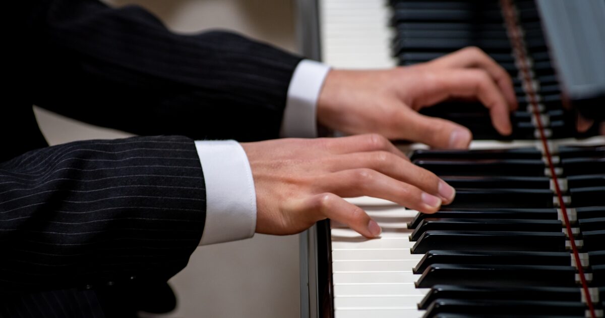 スーツを着た人がピアノを演奏している手元