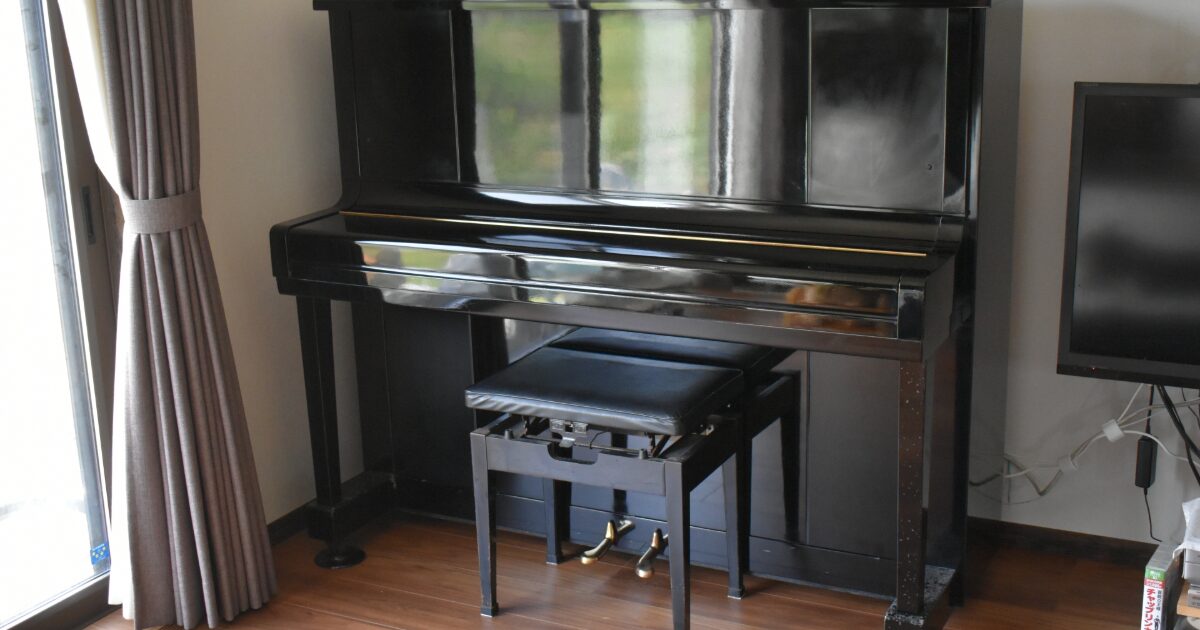 窓際に設置された黒いアップライトピアノと椅子