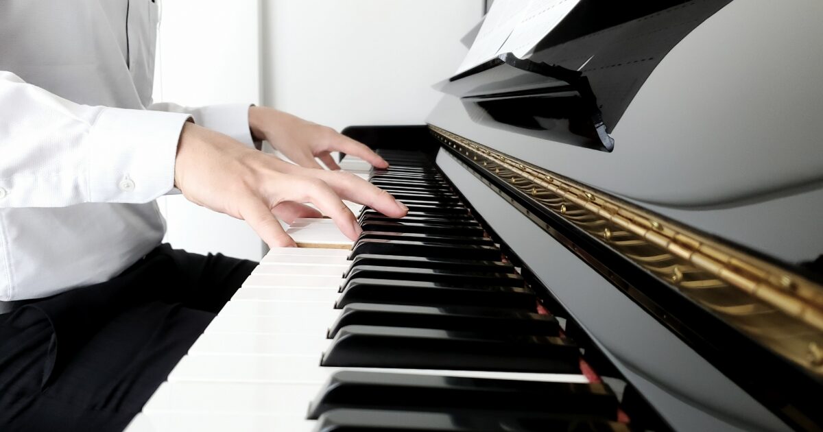 白いシャツの人がアップライトピアノを演奏している様子