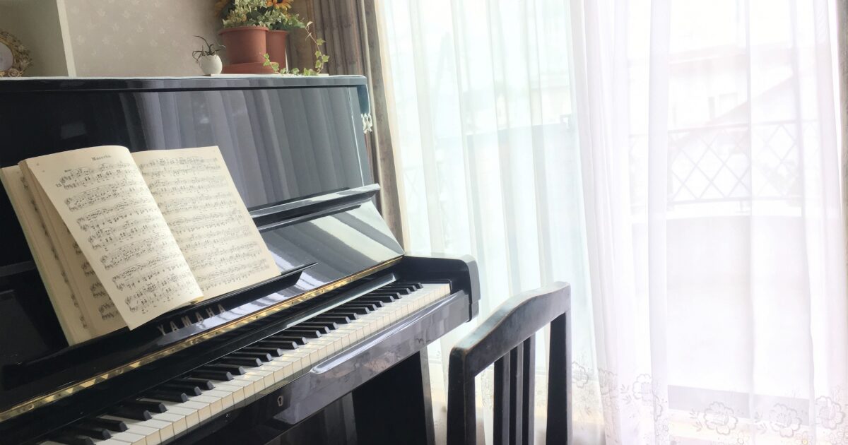 楽譜が置かれたアップライトピアノと窓辺の明るい部屋