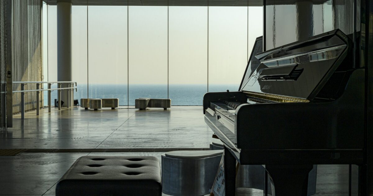 海の見える近代的な空間に置かれたアップライトピアノ