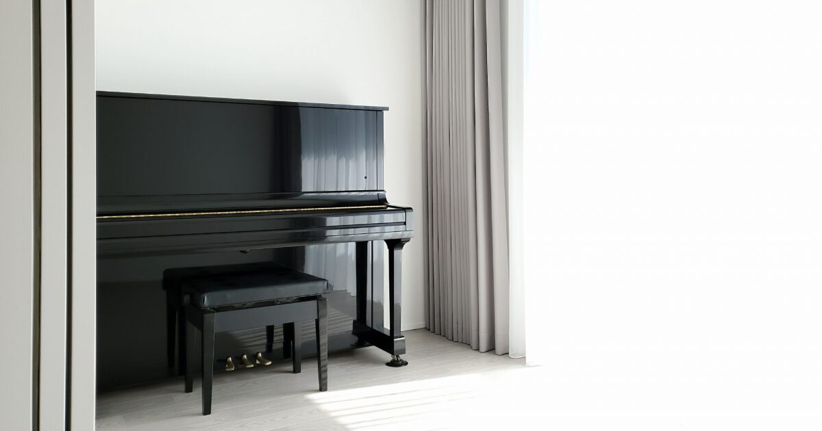 白い部屋に置かれた黒いアップライトピアノと椅子